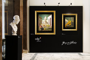 Allestimento di una mostra in una sala museale con busti su piedistalli e due opere incorniciate su parete scura, viste da vicino.