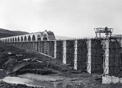 Ponte ferroviario in costruzione con arcate, impalcature e cantiere sul terreno sottostante