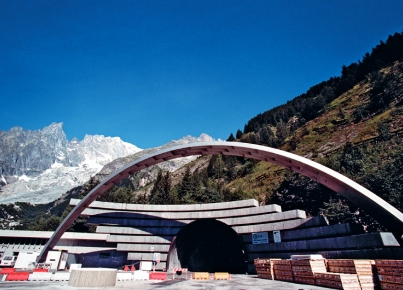 Arco strutturale davanti a un tunnel ai piedi di una montagna innevata.