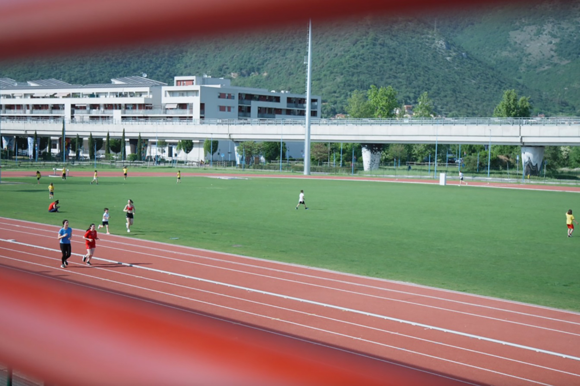 Pista di atletica all’aperto con due runner in corsia e campo verde sullo sfondo.