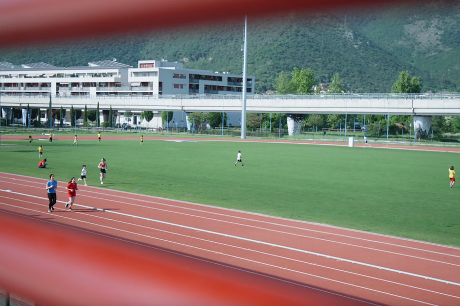 Pista di atletica all’aperto con due runner in corsia e campo verde sullo sfondo.