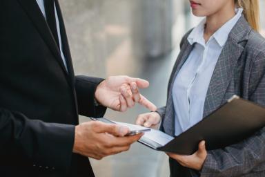 Collaborazione in ufficio: una persona consegna un documento mentre due professionisti parlano.