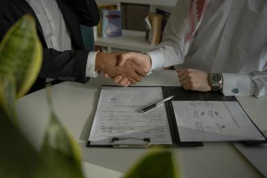 Stretta di mano durante una riunione di lavoro su un tavolo con documenti e penna.