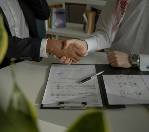 Stretta di mano durante una riunione di lavoro su un tavolo con documenti e penna.