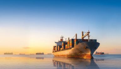 Nave cargo in navigazione nelle acque al tramonto, con riflessi sull’acqua.