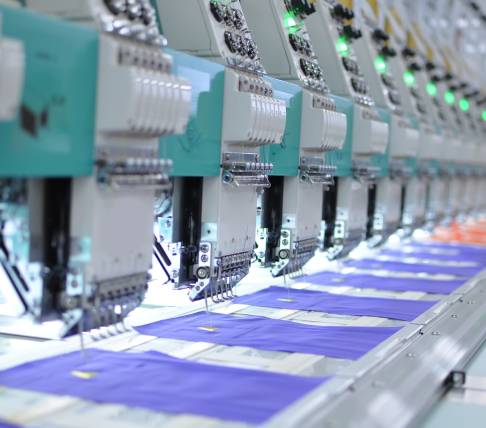 Fila di macchine industriali per ricamo automatico in funzione su tessuti viola.