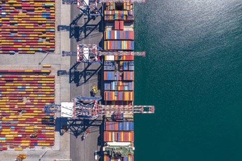 Vista aerea di una diga/porto con container colorati impilati e acqua sul lato.