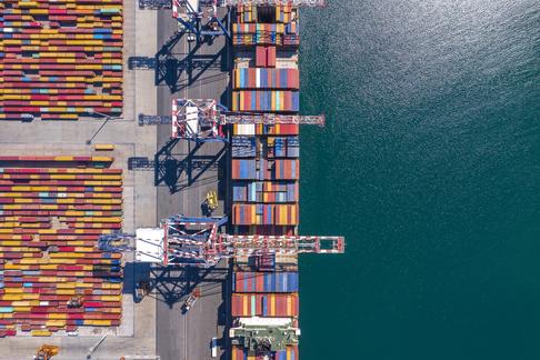 Vista aerea di una diga/porto con container colorati impilati e acqua sul lato.