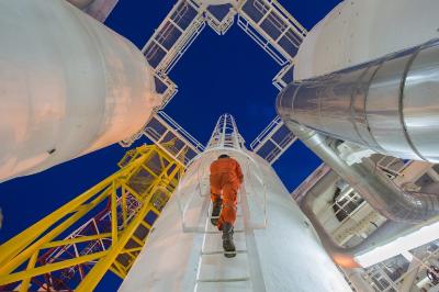 Astronauta su un ponte di lancio, con razzi e strutture metalliche contro un cielo blu.