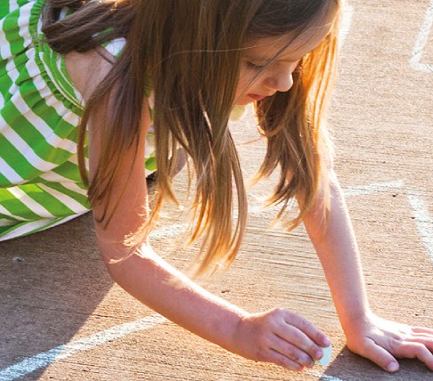 Bambina che disegna con il gesso sul pavimento in una giornata di sole.
