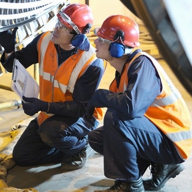 Due tecnici in tute di sicurezza lavorano in una galleria industriale, indossando elmetti e respiratori