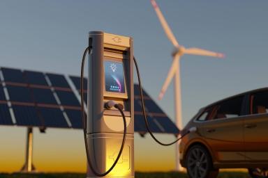 Stazione di ricarica per auto elettriche vicino a pannelli solari, con un’auto in sosta e pale eoliche sullo sfondo.