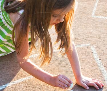 Bambina che disegna con il gesso sul pavimento in una giornata di sole.