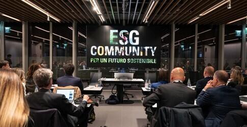 Sala conferenze con un palco e il logo “ESG Community”: relatore davanti a un pubblico seduto davanti a laptop.
