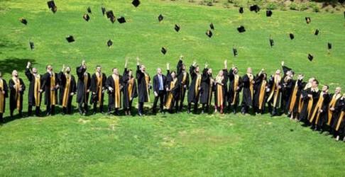 Foto di una cerimonia di laurea con una fila di studenti che lanciano i cappelli in aria in un prato.
