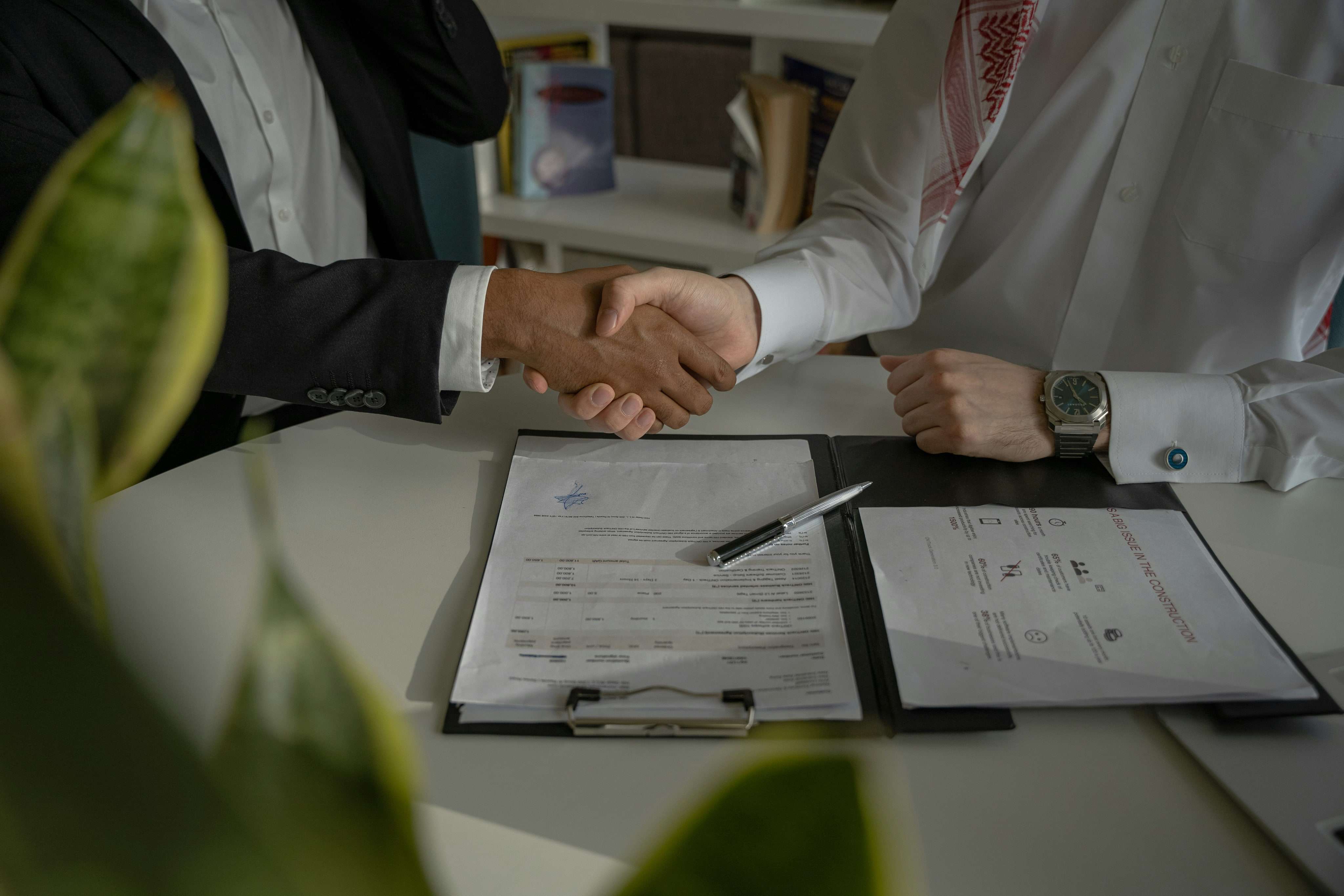 Due persone si stringono la mano sopra un contratto su un tavolo durante un incontro di lavoro.