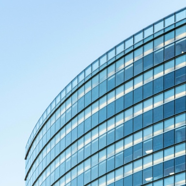 Veduta tra due ali di un edificio moderno con facciate vetrate, finestre verticali e riflessi blu.