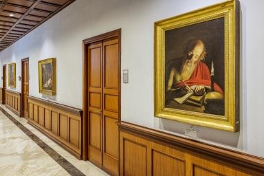 Corridoio di un museo con quadri alle pareti e pavimento in pietra.