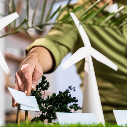 Mano che posiziona un piccolo pannello solare in un modello in scala di un paesaggio di energia verde con turbine e alberi