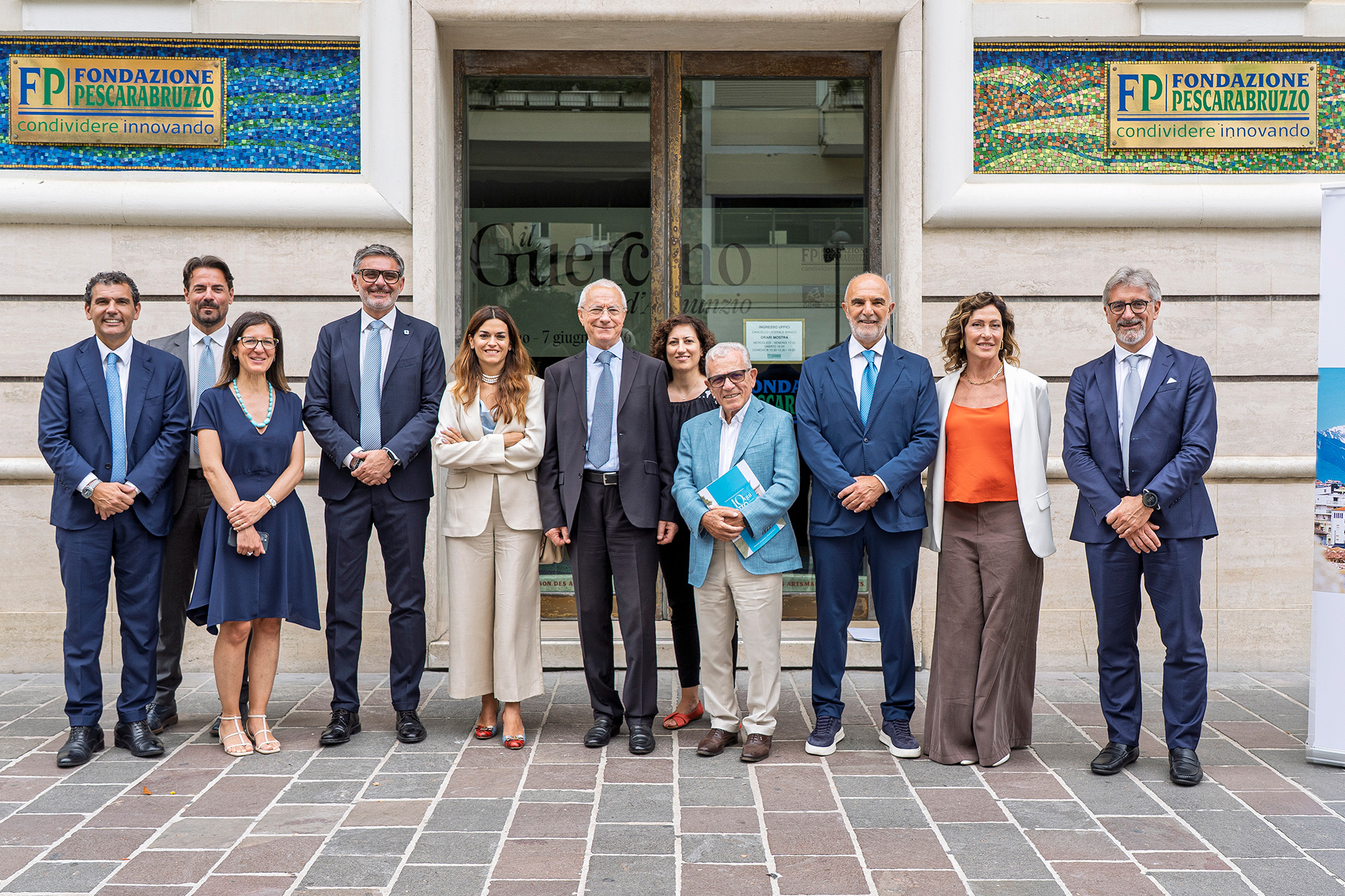 Gruppo di persone in posa davanti a un edificio, davanti a targhe e insegne di fondazione pescarabruzzo.