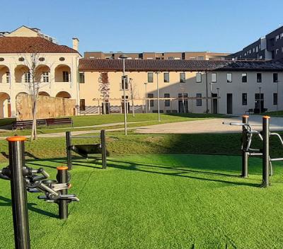 Giardino verde curato con attrezzature per l’allenamento all’aperto, circondato da edifici storici e moderni.