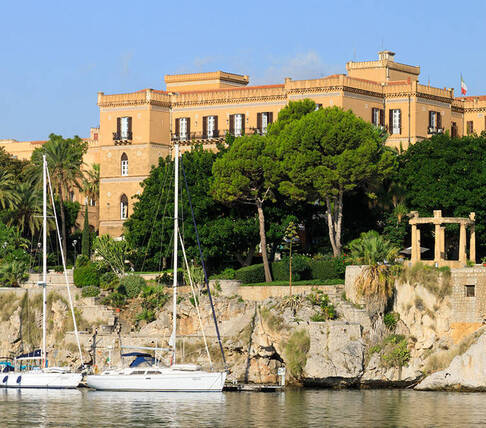 Panorama del lungomare con yacht, scogliera e palazzi storici sullo sfondo.