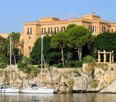 Panorama del lungomare con yacht, scogliera e palazzi storici sullo sfondo.