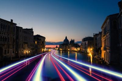 Canale veneziano al crepuscolo con luci dei veicoli in scia e la Basilica di Santa Maria della Salute sullo sfondo.