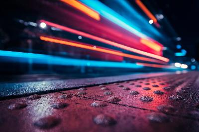 Primo piano di una strada bagnata con scie luminose colorate dovute al traffico in movimento.