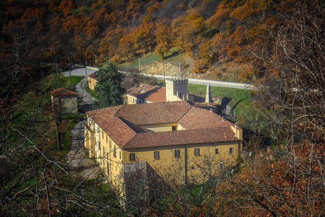 Antico monastero giallo con tetti in terracotta immerso nei boschi autunnali.