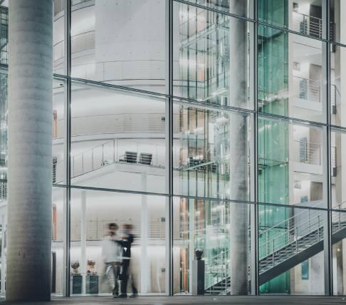 Interno di un edificio moderno con uffici e corridoi, visti attraverso vetrate e strutture in metallo