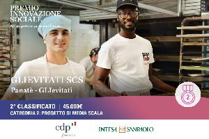 Due giovani sorridenti lavorano in una cucina industriale; sullo sfondo scaffali e una grafica del “Premio Innovazione Sociale” con “2° classificato”.