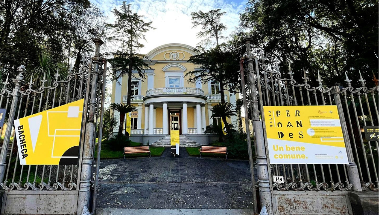 Ingresso di un edificio storico con cancelli decorati e grandi cartelli gialli.