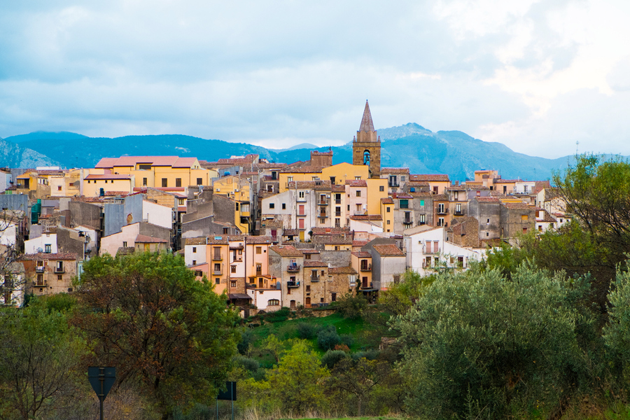 Panorama di un borgo con case e campanile sullo sfondo delle montagne.